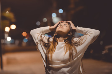 Young emotional woman looking up, city street in the night, evening lights bokeh background...