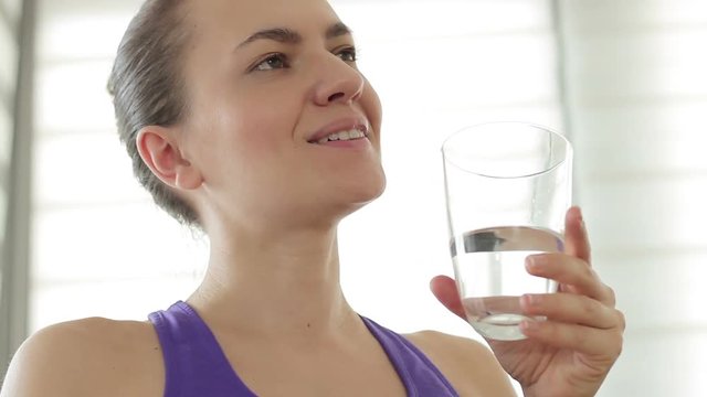 Portrait of young cheerful sporty woman drinking fresh and pure water from glass, close up
