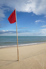 warning sign of a red flag at a beautiful clean beach with a blue sky and cloud in background