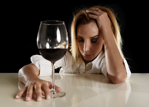 drunk alcoholic blond woman alone in wasted depressed drinking red wine glass suffering hangover