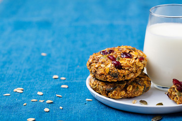 Pumpkin, oat cookies with cranberries, maple glaze and glass of milk on a blue textile background.