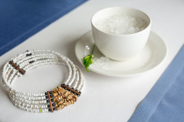 Fototapeta na wymiar cup of refined sugar and a necklace on white- blue background
