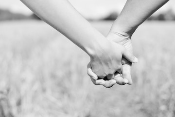 Closeup black white photography on male and female holding hands outdoors over a field of wheat