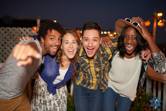 Multi-ethnic millenial group of friends taking a flash selfie photo with mobile phone on rooftop terrasse at night time