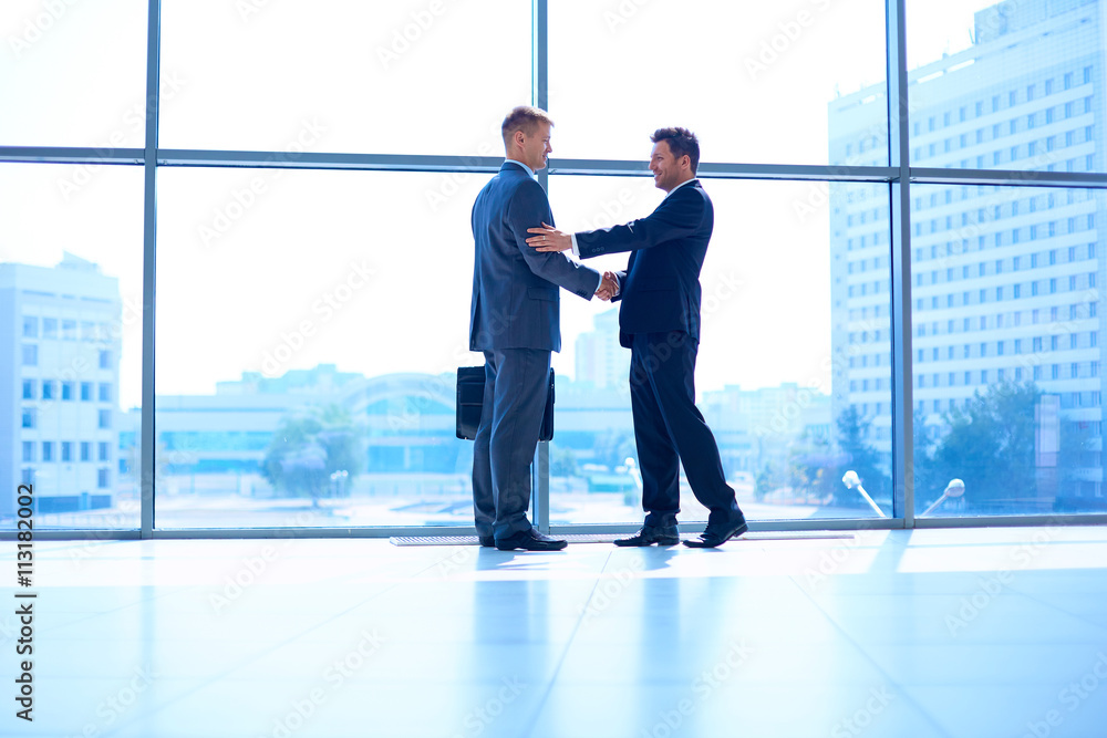 Wall mural Full length image of two successful business men shaking hands with each other