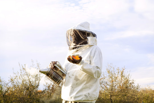 Beekeeper with smoker and honey bottle standing in field