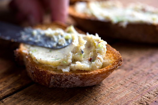 Person spreading green garlic pate on crostini
