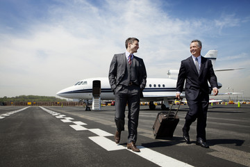 Two businessmen walking away from jet plane along runway