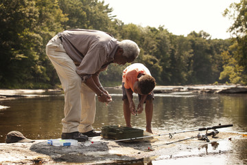 Grandfather and grandson with fishing equipment at riverbank
