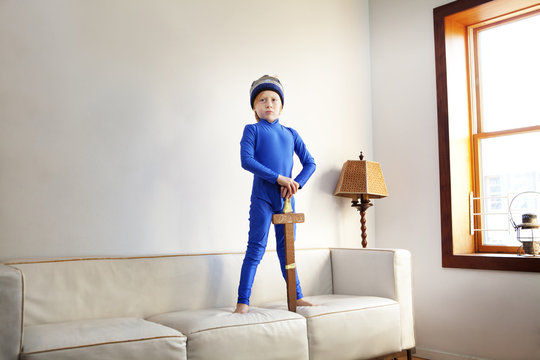 Boy holding wooden sword while standing on sofa at home