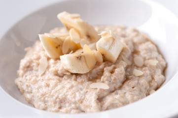 oatmeal porridge with banana  slices and almonds close-up on white plate
