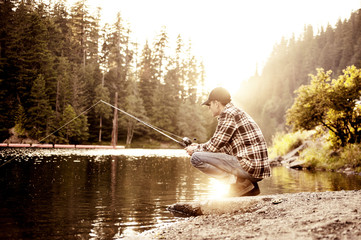 Young man fishing in lake at sunset