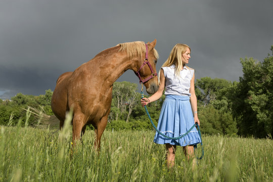 Cowgirl and horse standing in grazing field