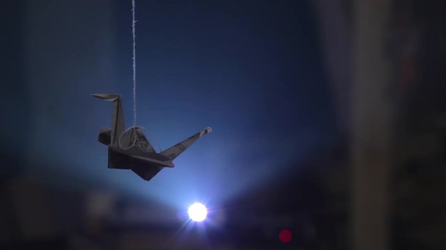 Paper origami crane hanging on thread against bright light of projector
