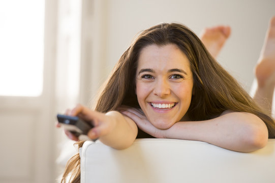 young beautiful woman lying on couch holding remote control watching television happy and relaxed