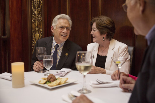 Smiling Senior Friends Talking With Each Other While Sitting In Restaurant