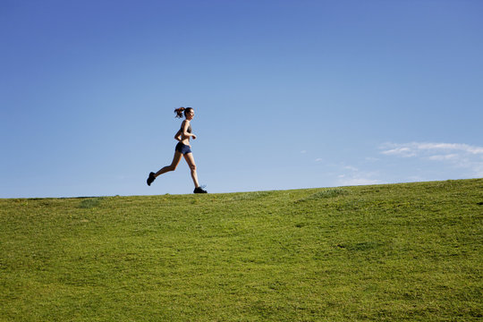 Woman running on grassy field against blue sky
