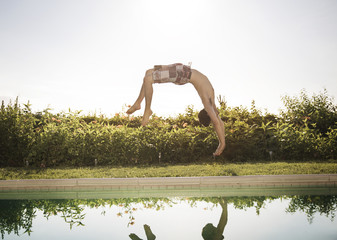 Man somersaulting into swimming pool against clear sky