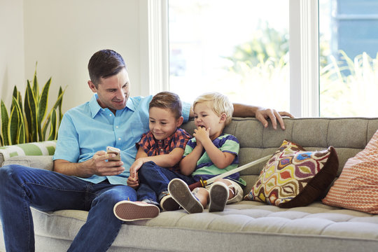Man sitting with sons on sofa while looking at mobile phone