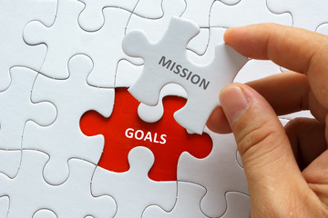 Hand holding piece of jigsaw puzzle with word MISSION GOALS.