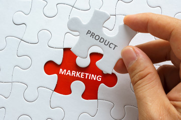 Hand holding piece of jigsaw puzzle with word PRODUCT MARKETING.