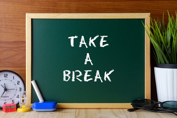 Words TAKE A BREAK written on green chalk board on wooden table.