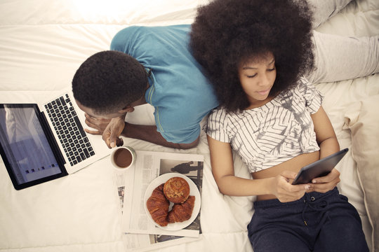Young couple lying on bed while having breakfast