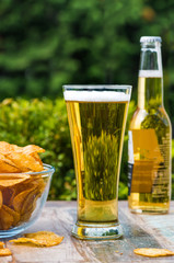 A glass of beer and a bowl of crisps on a table in the garden