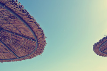 Low angle view on two straw parasols on the beach, on a sunny day, with blue sky in the middle. Can be used as summer background. Image filtered in faded, retro, Instagram style. Copy space. - 113207490