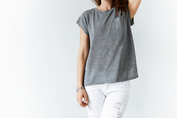 Portrait of young female in denim pants and white casual gray T-shirt posing against white studio wall background with copy space for your text or advertising content, holding a hand behind her head