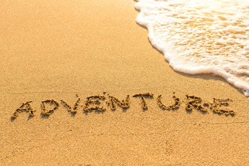 Adventure - inscription on sand beach with the soft wave.