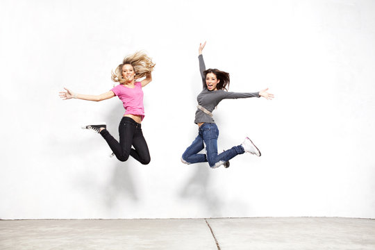 Portrait Of Women Jumping While Looking Away Against Wall