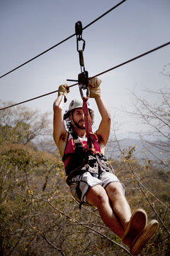 Man zip lining against sky in forest
