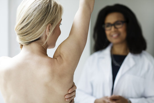 Naked woman with raised arm and doctor in background,