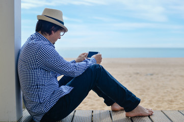Person sitting near the sea with mobile smartphone. back side view of barefoot man