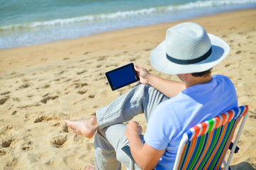 Business man using tablet computer, tropical beach outdoors. Back view