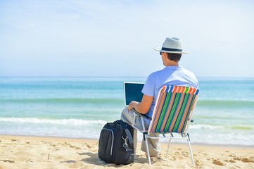 Back view of man with laptop on beautiful sandy beach island vacation