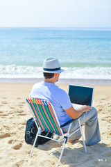 Back view of man with laptop on beautiful sandy beach island vacation