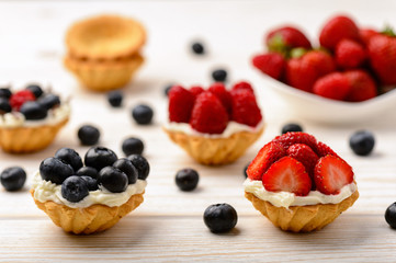 Tartlets with cream, blueberries, raspberries and strawberries on white wooden table. Selective focus.