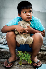 Boy poor with old teddy bear sitting on old wood pile