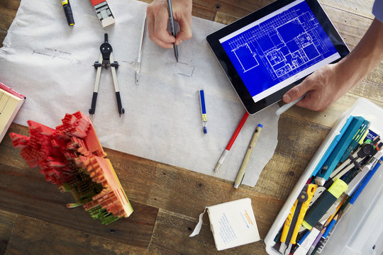 Cropped image of architect drawing blueprints while holding tablet computer at office