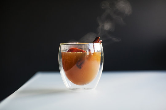 A steaming hot glass of apple cider with an apple slice and cinnamon stick