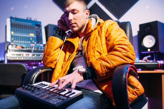 Musician playing on synthesizer at studio. Front view on dj in yellow coat creating music on synthesizer and listening to it in headphones. Closeup of playing music dj