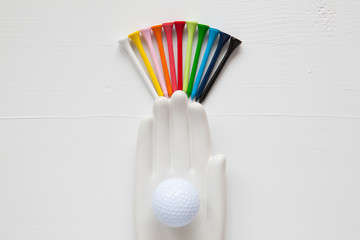 Detail of ceramic hand with golf balls and tees on the white woo