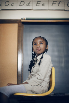Thoughtful girl sitting on the yellow chair in the classroom