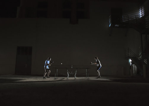 Two men playing table tennis at night