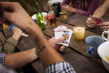 Cropped image of friends playing cards at picnic table in forest