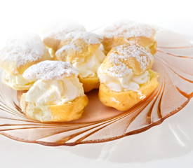 Cream puff or profiterole with filling and powdered sugar topping, isolated, against white background