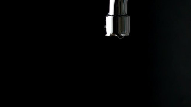 Dripping chrome water tap against black background slow motion shot