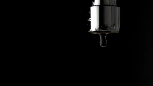 Macro slow motion shot of dripping chrome water tap against black background